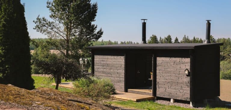 Tumma hirsinen piharakennus pellon laidalla