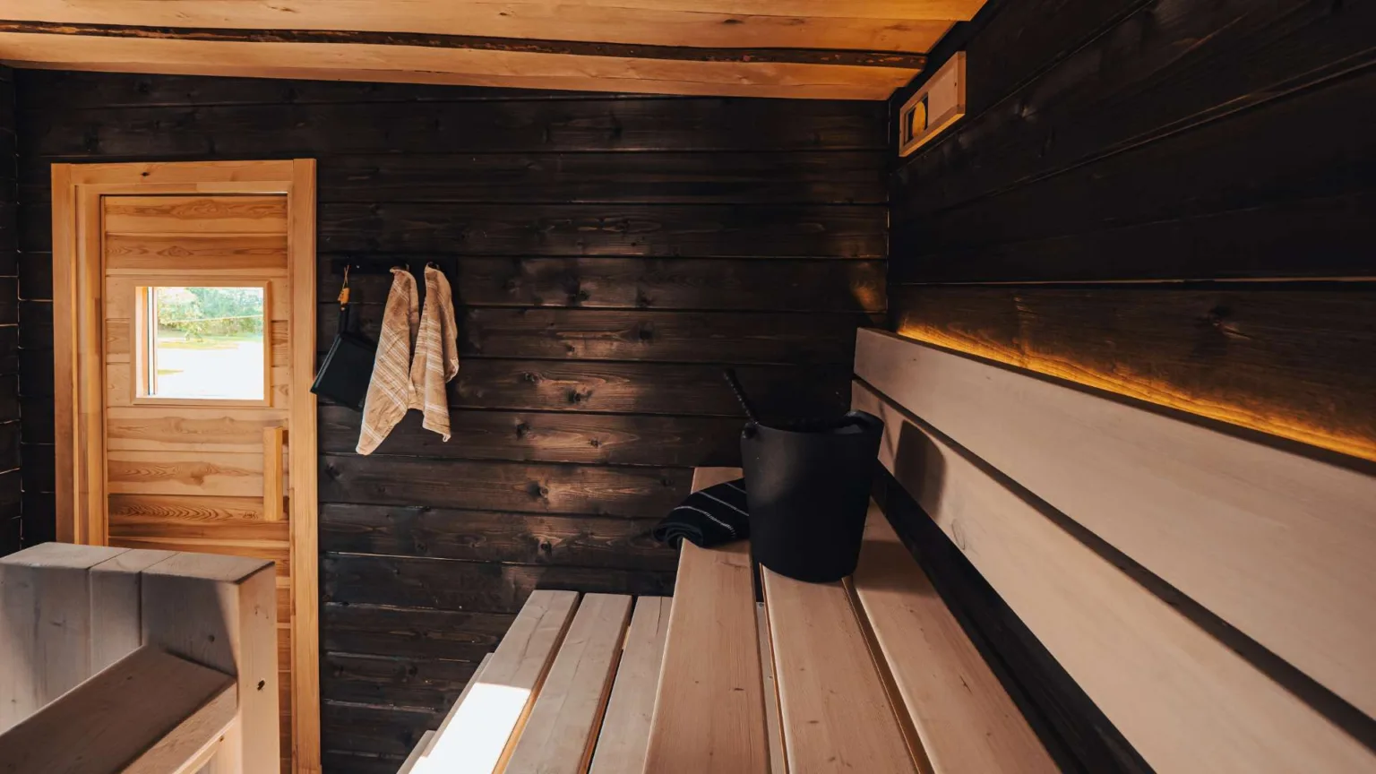 Tervas-hirsisauna tummilla seinillä ja vaaleilla lauteilla.