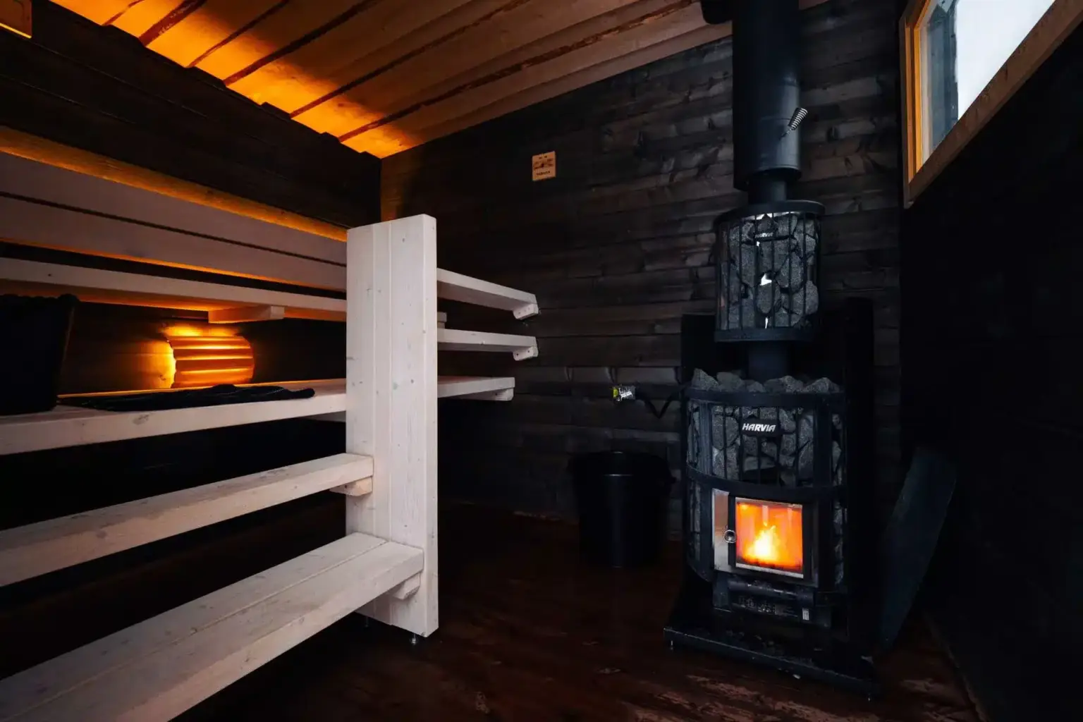 Tumma sauna, jossa puulämmitteinen kiuas ja vaaleat lauteet